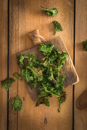 Kale chips with sea salt in on old wooden cutting boardの写真素材
