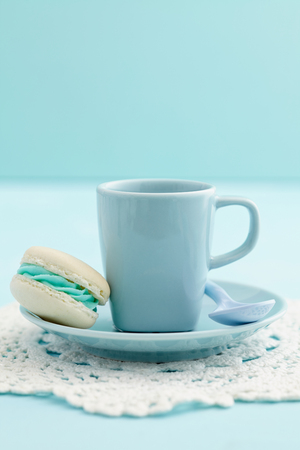 Cup of coffe with a turquoise macaron with buttercream fillingの写真素材