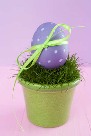 Purple Easter egg with polka dots with a bow in a flowerpot with grassの写真素材