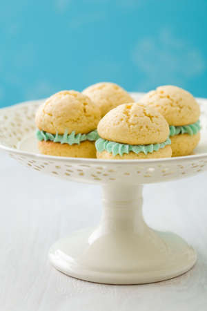 Vanilla whoopie pies with turquoise buttercream filling on cake standの写真素材