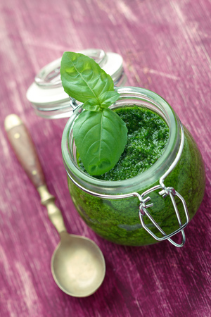 Pesto in a glass jar with a spoon on pink wooden tableの写真素材