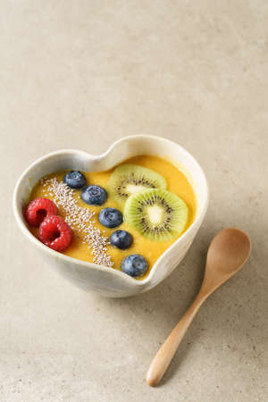 Peach smoothie bowl with blueberries, kiwi, white chia seeds and raspberries in a heart shaped bowlの写真素材