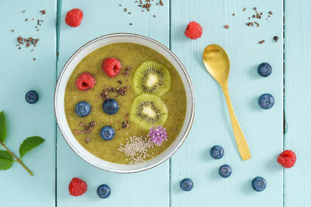 Kiwi smoothie bowl with blueberries, kiwi, white chia seeds, cocoa nibs and raspberries in a bowlの写真素材