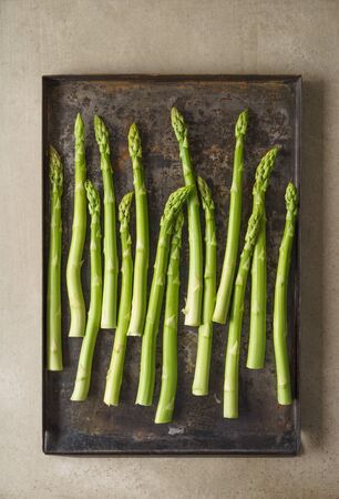 Fresh uncooked green asparagus on old rustic baking trayの写真素材