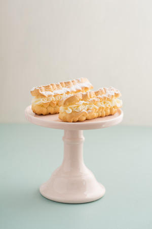Eclairs with buttercream filling on a pink cake standの写真素材