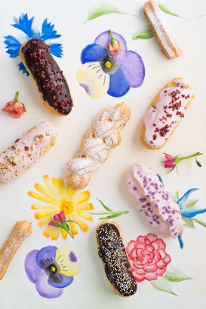 Eclairs with chocolate ganache and icing with different toppings on painted flowersの写真素材