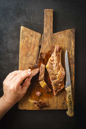 Man picking a piece of a seared dry aged rib eye steak from a wooden boardの写真素材