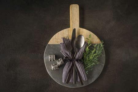 Christmas place setting with black silverware, fir greens and tiny gift parcels on wooden and slate...