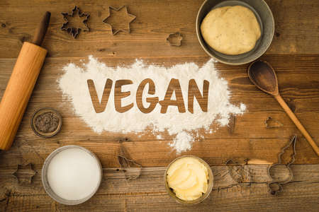 Flatlay collection of tools and ingredients for baking vegan Christmas cookies with margarine and chia seeds as egg replacement and the word vegan written in flour on a dark wooden table. Shot from aboveの写真素材