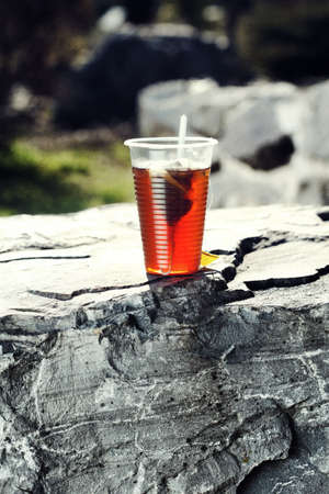 Plastic cup with tea on big stone over nature background.の写真素材