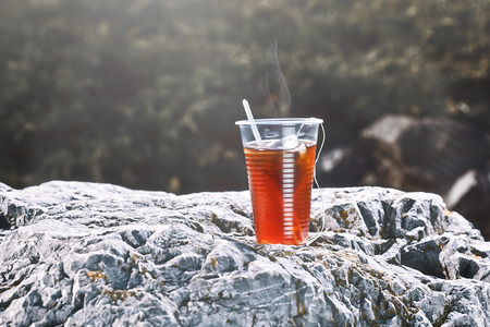 Plastic cup with tea on big stone over nature background.の写真素材