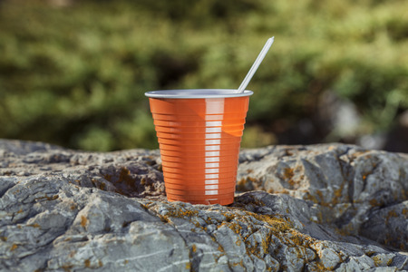 brown plastic coffee cup with a spoon on a rock on a background of forest landscape.の写真素材