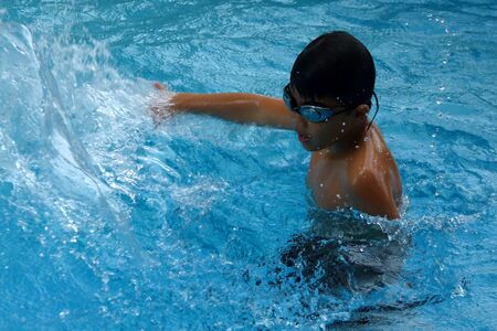 Asian kid play water in swimming pool - boy portrait with splashの写真素材