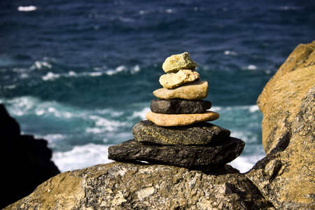 A pile of 7 stones forming a pyramid triangle shape sit on a rock on front of the ocean peacefullyの写真素材