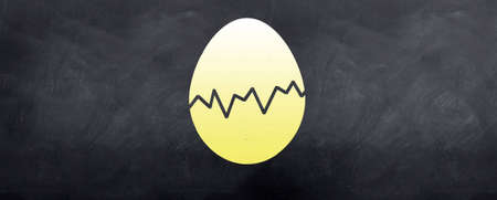 A yellow cracked easter egg is sketched on the blackboardの写真素材