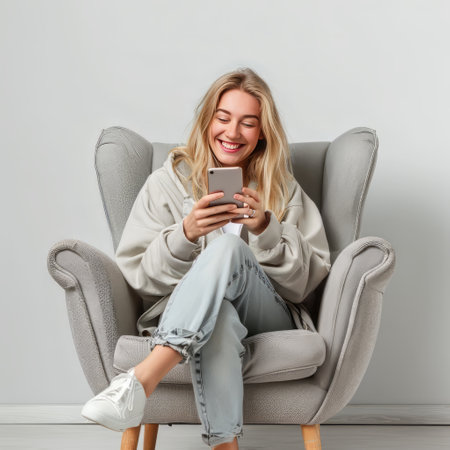Portrait of a happy young woman using mobile phone while sitting in armchair regenerative aiの素材