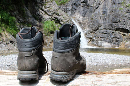 Mountain boots on a log with a waterfall in the backgroundの写真素材