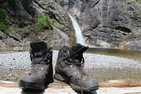 Mountain boots on a log with a waterfall in the backgroundの写真素材