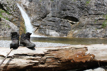 Mountain boots on a log with a waterfall in the backgroundの写真素材