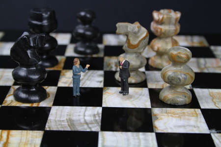 Chess board with small figures of business people and chess pieces in the backgroundの写真素材