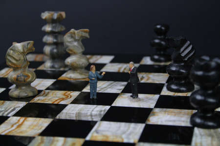 Chess board with small figures of business people and chess pieces in the background
