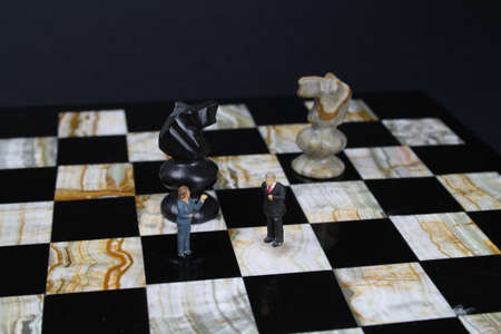 Chess board with small figures of business people and chess pieces in the backgroundの写真素材