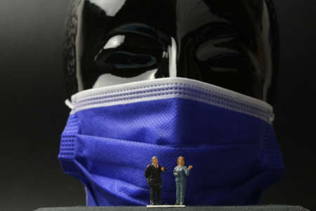 small figures in front of a large black head with protective maskの写真素材
