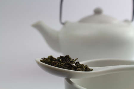Asian teapot in white with fresh green tea in the foregroundの写真素材