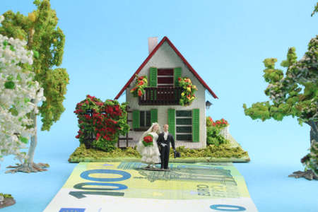 small model house with figures of a bridal couple standing on a banknote in front of the house