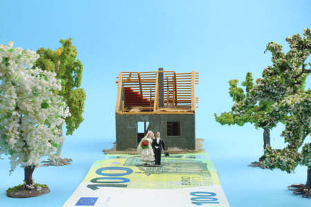 small model house with figures of a bridal couple standing on a banknote in front of the houseの写真素材