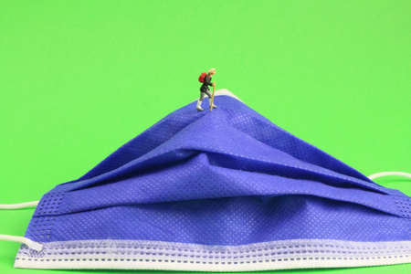 Face mask with small figures symbolizes the difficult way out of the crisis with a green backgroundの写真素材