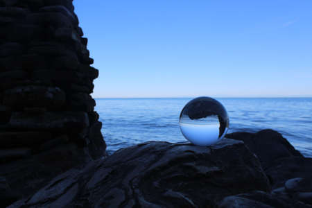 Glass ball lies on a stone by the sea with the horizon in the backgroundの写真素材