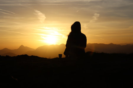 Young woman is sitting on a mountain during sunriseの写真素材