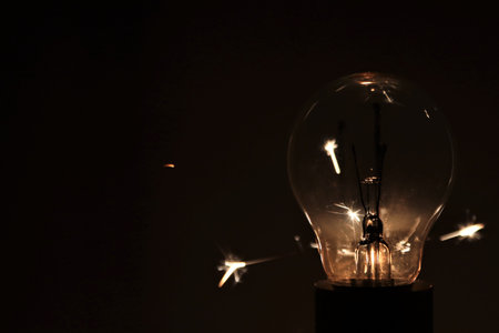 Incandescent Edison light bulb glowing in the dark with sparks.の写真素材