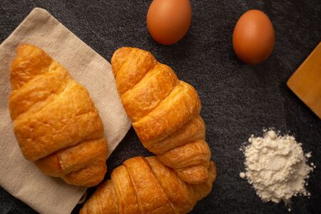 Croissants with white coffee cups with flour and eggs on a black background, breakfast, brown bread, morning drinks Concept: Delicious food for health, pastry, bakery, restaurant, lifestyle areaの写真素材