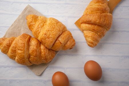 Croissants with coffee cups with flour and eggs on a white background, breakfast, brown bread, morning drinks, fantasy world: delicious food for health, pastries, bakery, restaurants, lifestyle areasの写真素材