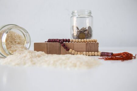 ZAKAT donation for Muslim according to religious principles during the Ramadan month, concept: rice grain in bow and rosary on a white tableの写真素材