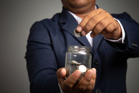 Businessman hand with putting money coins in the officeconcept: Saving money wealth and financial Personal, finance management  loan for a home,
 diagram chart earnings to plan profitの写真素材