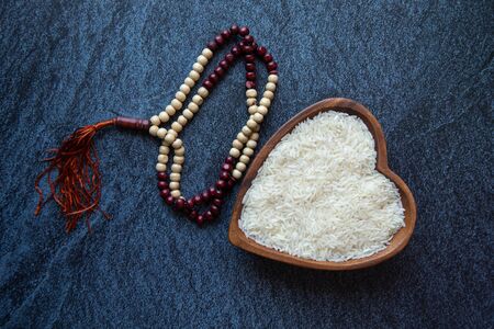 ZAKAT donation for Muslim according to religious principles during the Ramadan month, concept: rice grain in bow and rosary on black backgroundの写真素材