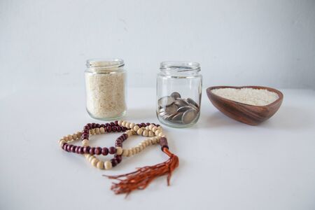 ZAKAT donation for Muslim according to religious principles during the Ramadan month, concept: rice grain in bow and rosary on a white tableの写真素材