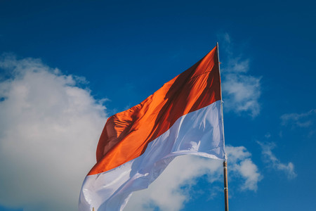 Indonesia flag on the woonden mast on blue sky background