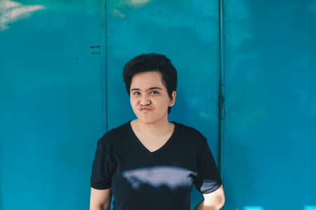 Asian beautiful short hair girl on blue background with funny and disgusting face expressionの写真素材
