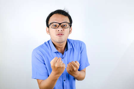 Young Asian Man wear blue shirt is funny angry face with shouting and pointing finger at camera isolated over white backgroundの写真素材