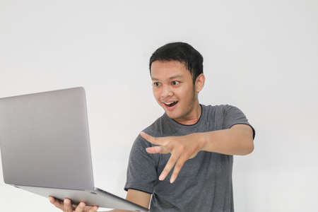 Young Asian man in grey t-shirt Feeling happy and smile with holding laptop in hand.