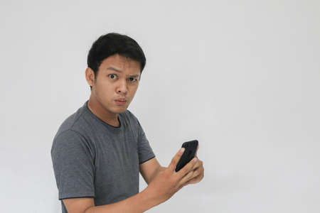 Wow face of Your Asian man shocked what he see in the smartphone on isolated grey background.
