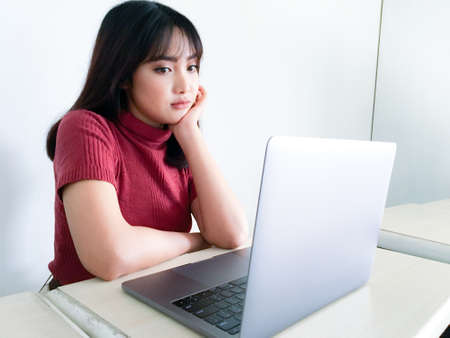 Asian beautiful hair girl is confuse or bored in the front of laptop on the isolated white backgroundの写真素材