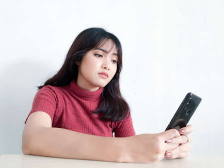 Asian beautiful girl is reflect and think by looking outward in the smartphone on the isolated white backgroundの写真素材