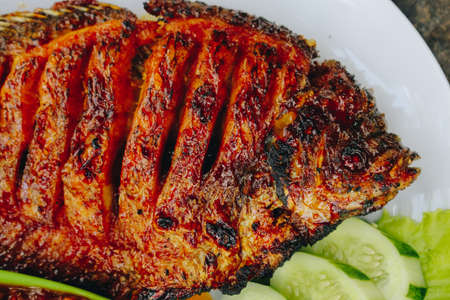 Delicious grilled tilapia (nila bakar) from indonesia with rice, tempeh, vegetables, and chilli sauce in plateの写真素材