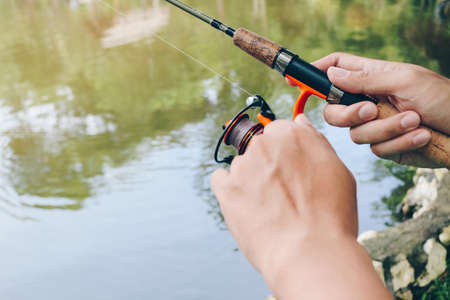 Close up of spinning with the fishing reel in the hand, fishing hook on the line with the bait in...
