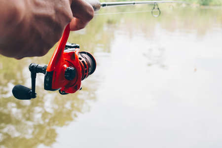 Close up of spinning with the fishing reel in the hand, fishing hook on the line with the bait in the left hand against the background of the water.の写真素材